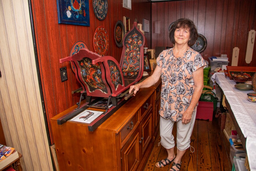 A woman standing next to a hand-painted sleigh that is sitting on top of a wooden cabinet.