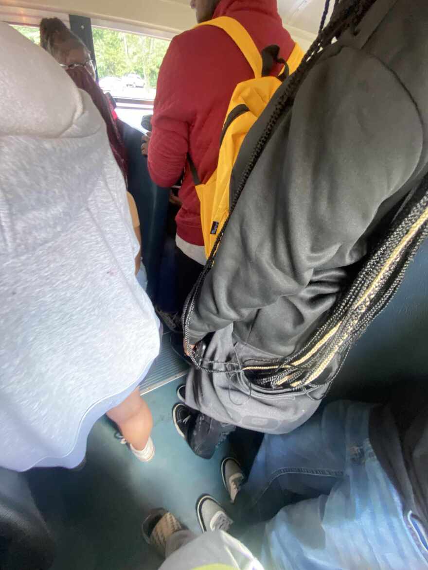 Photo taken from inside a school bus shows students standing in the aisle.