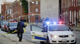 In this July 30, 2015 picture, a member of the Baltimore Police Department removes crime scene tape from a corner where a victim of a shooting was discovered in Baltimore. (Patrick Semansky/AP)