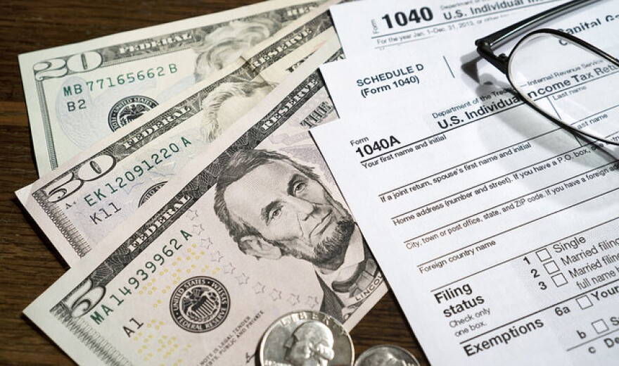 A close up shot of money, tax forms, and a pair of glasses.