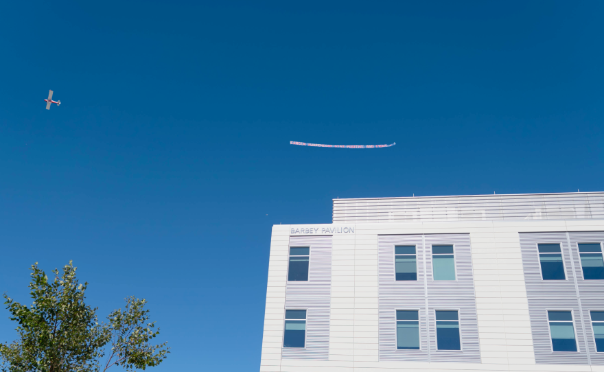 A biplane tows a banner over Cape Cod Hospital in Hyannis with the message "Cancer Awareness. Stay Positive And Fight."