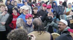 In this Friday, Jan. 18, 2019 image made from video provided by the Survival Media Agency, Covington Catholic studen Nicholas Sandmann, center left, stands in front of an elderly Native American singing and playing a drum in Washington.
