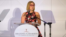 Woman in floral dress speaks at podium