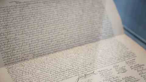 Close-up view through a case of a slightly browned paper with writing in tidy cursive and many signatures at the bottom, including, most prominently, John Hancock's.