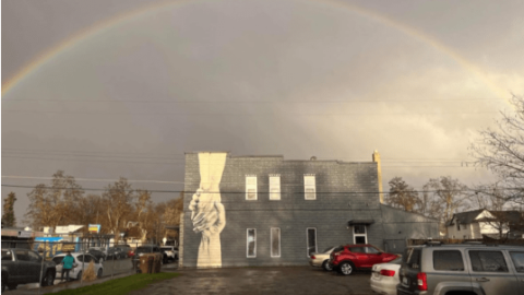 A building in the rain with a picture of two hands clasping painted on its side.