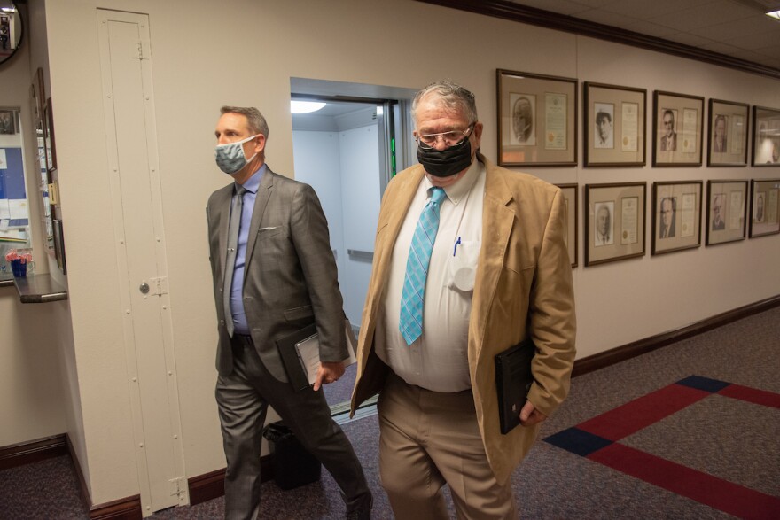 State Senators Scott Hammond walk down the hall. They are wearing masks and carrying portfolios.