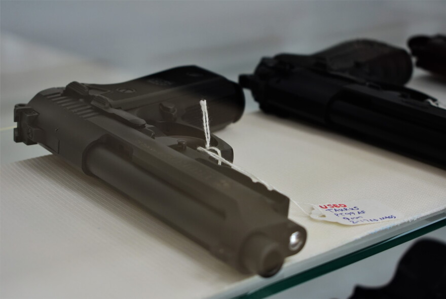 A black gun sits on its side on a shelf next to another gun 