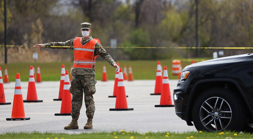 A worker at the state-run coronavirus testing site at Monroe Community College's campus in Brighton directs a driver through the parking lot.