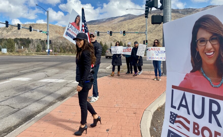 Boebert waves an American flag and greets drivers on the corner of Willits Lane and Highway 82 in Basalt. Behind her, various residents of the Roaring Fork Valley carry signs that express their support of Adam Frisch and their disappointment in her performance as a representative.