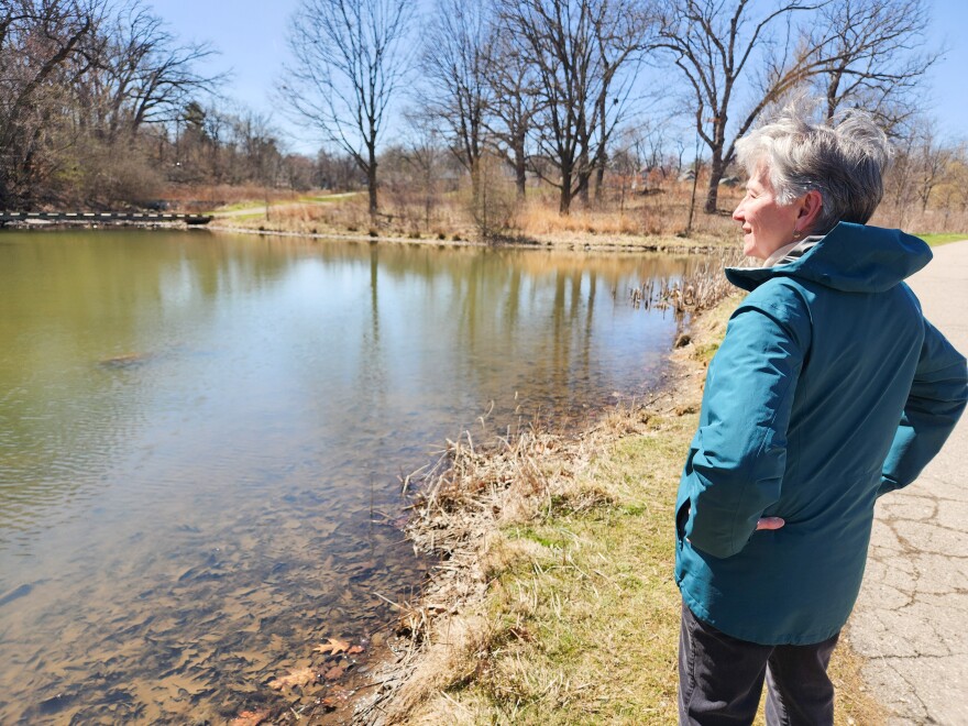 A photo of an older woman in a teal jacket overlooking a small pond. 
