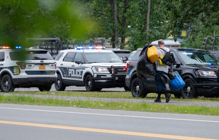 A man carries his belongings near police vehicles.