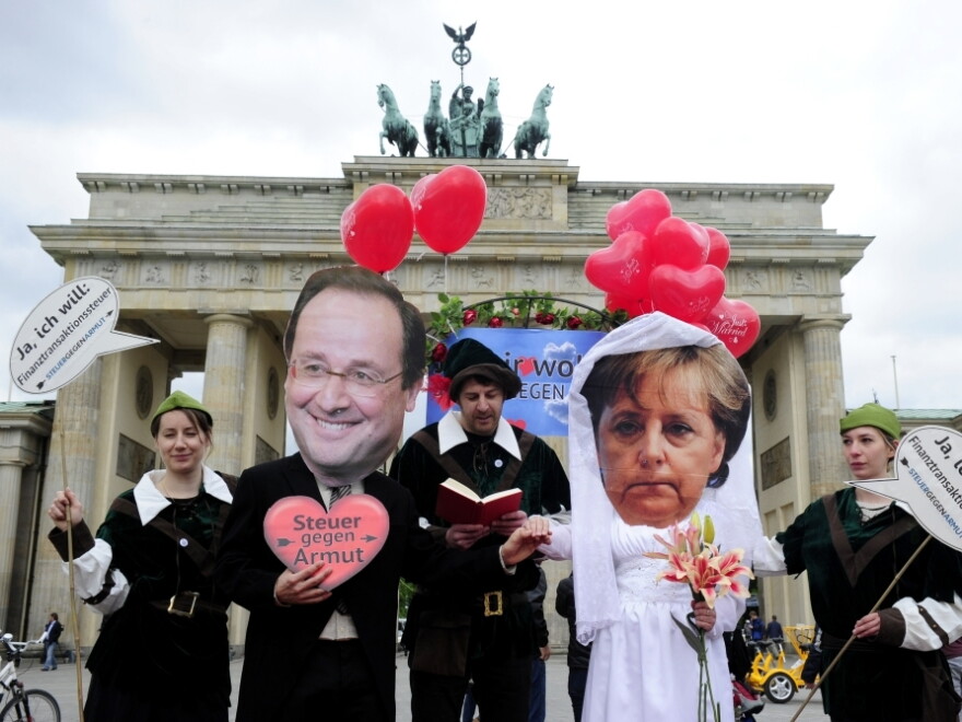 Activists wear masks featuring German chancellor Angela Merkel and incoming French socialist president Francois Hollande as they perform a fake marriage in front of the Brandenburg Gate in Berlin, on May 7, 2012.