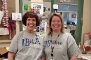 A woman with short brown hair standing next to a woman with shoulder-length blonde hair. They're smiling into the camera and wearing gray t-shirts that say I Believe
