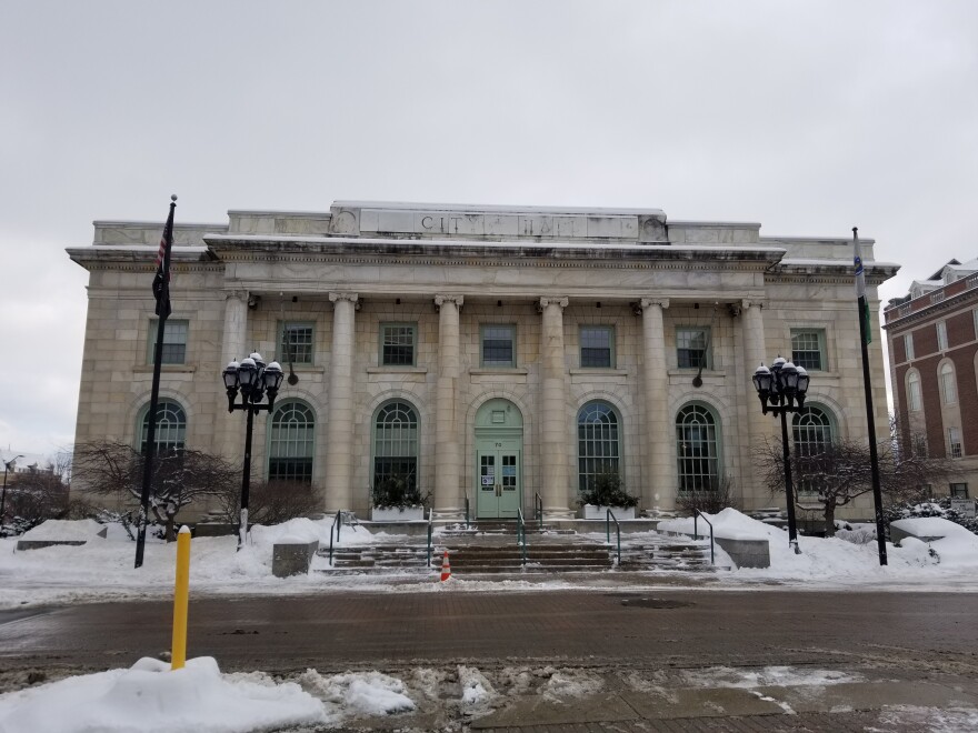 A stone building with a colonnade sits below a grey sky amid snowdrifts.