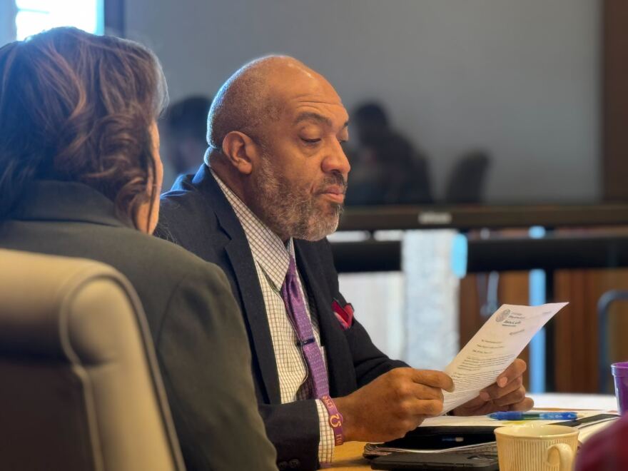 A man in a suit reviews a documents while seated at a desk. 