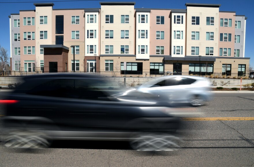 Cars drive past an apartment complex