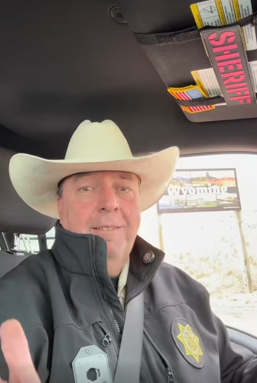 In a Facebook post, the sheriff sits in a truck cab with a white cowboy hat on, in the background is the Wyoming state welcome sign.