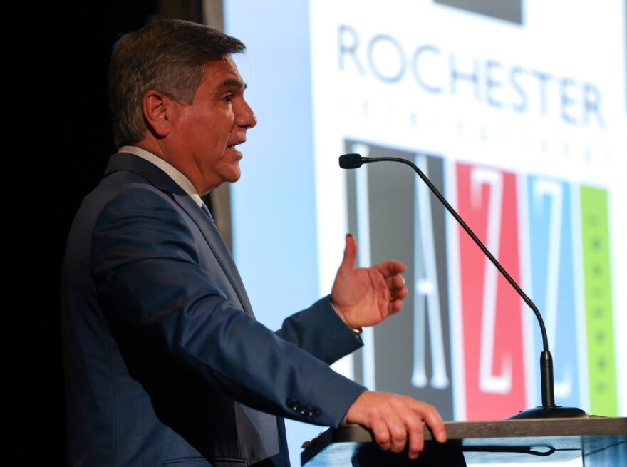 Profile of Iacona speaking in front of a screen with the Rochester jazz festival logo