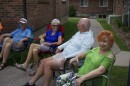 Four senior citizens sit on lawn chairs outside a cluster of small apartment buildings.