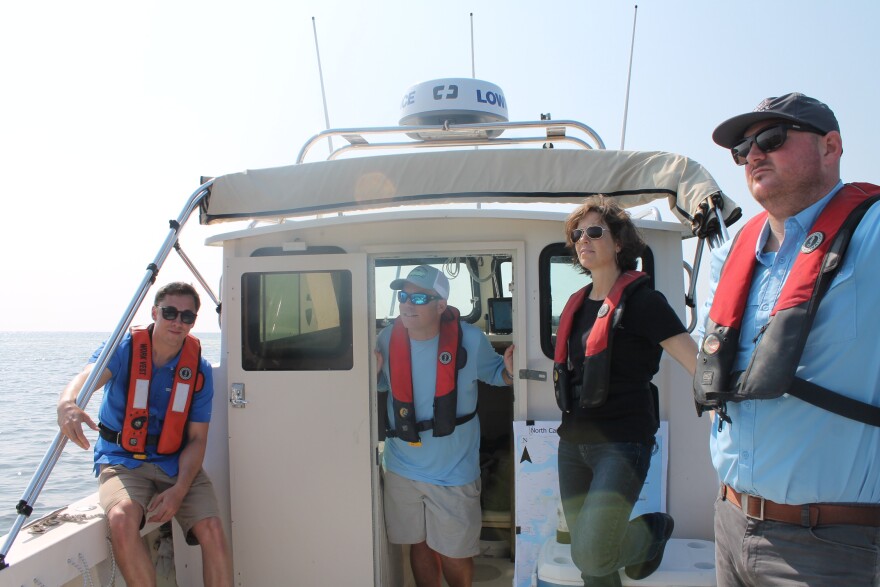  People from the NC Coastal Federation, state division of marine fisheries and a local contractor look on from a small boat as the crew tosses the last few rocks to complete the sanctuary.