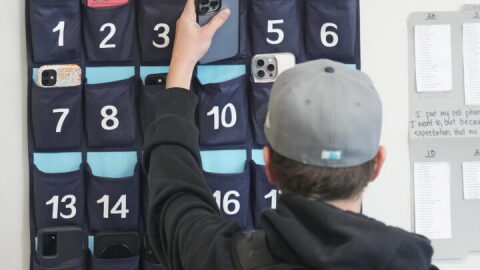 A ninth grader places his cellphone into a phone holder as he enters class at Delta High School, Friday, Feb. 23, 2024, in Delta, Utah. At the rural Utah school, there is a strict policy requiring students to check their phones at the door when entering every class. Each classroom has a cellphone storage unit that looks like an over-the-door shoe bag with three dozen smartphone-sized slots. 