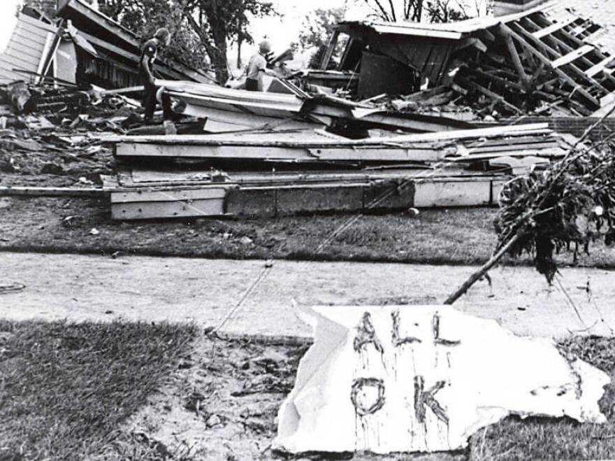 Two children climb over what remains of a home that has an "All OK" sign in front. The flood caused $165 million of damage to the area.