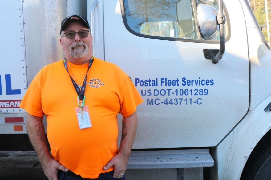 A person in an orange shirt and hat stands outside a white truck.