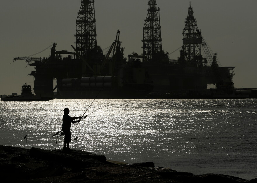 FILE - A man fishes near docked oil drilling platforms May 8, 2020, in Port Aransas, Texas. 