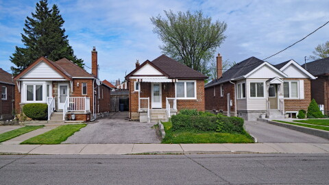 A row of modest brick homes lines a residential street. Each has a small front porch, driveway and neatly trimmed landscaping. The sky is partly cloudy.