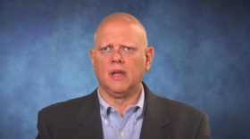 A head shot of former state Supreme Court Justice Matthew Rosenbaum, wearing a gray suit and blue shirt in front of a blue background
