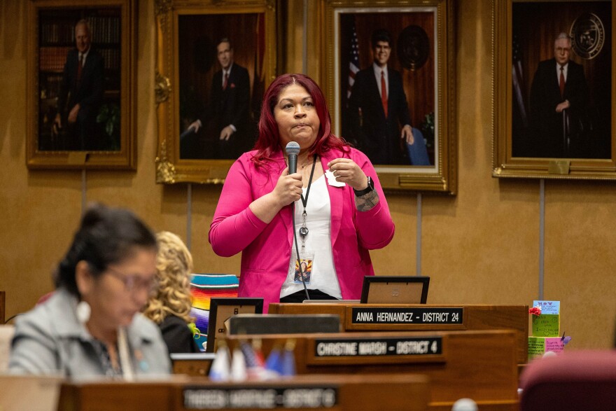 Woman in pink blazer speaks into microphone