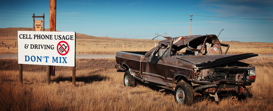 A totalled pickup truck sitting next to a sign that reads, "Cell Phone Usage and Driving Don't Mix."