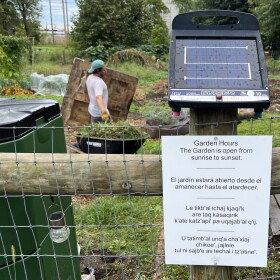 A sign posted to a fence announces the community garden hours in four languages.
