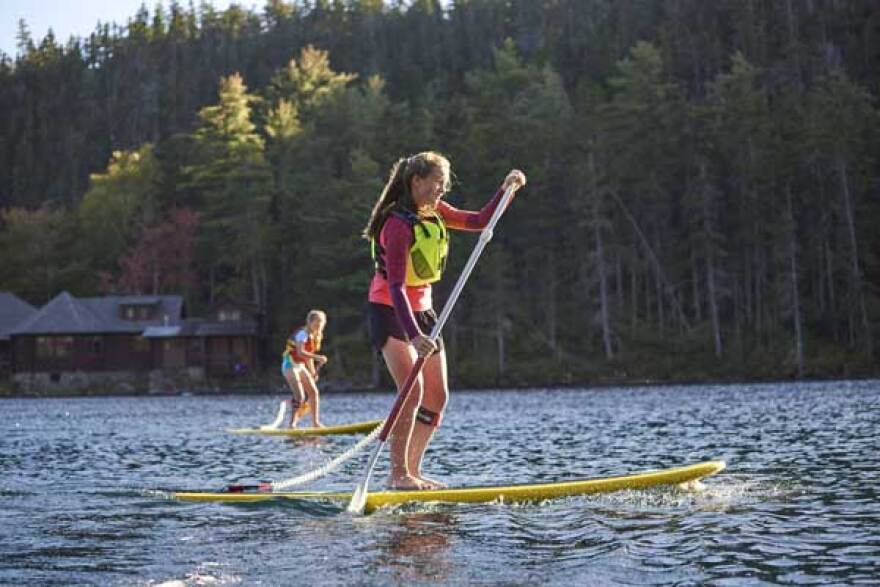 Two people stand-up paddle-boarding on a lake in Maine