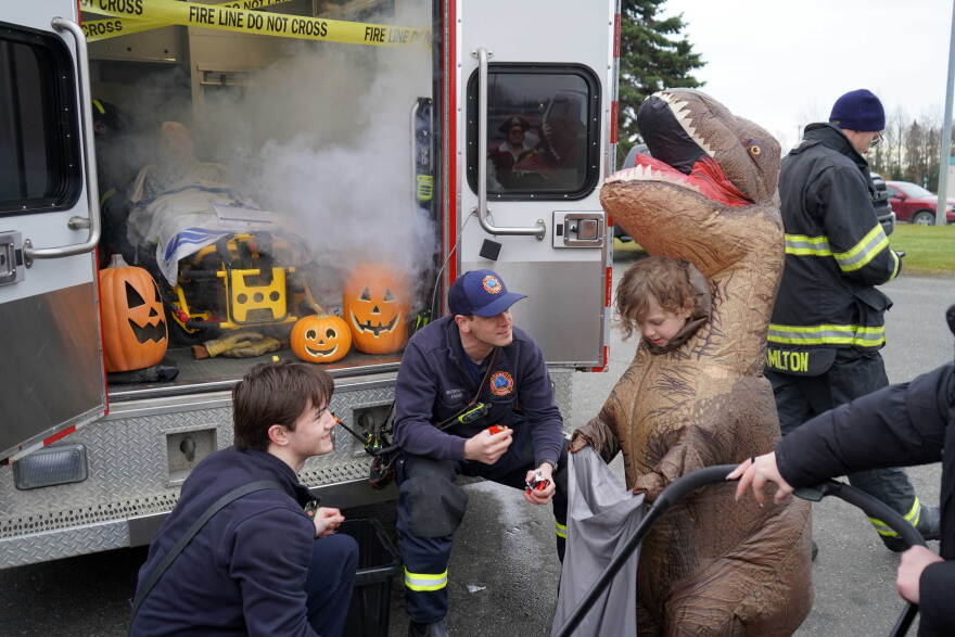 Staff from Kenai Fire Department fill a dinosaur's bag with candy at the Trunk-or-Treat hosted by the Boys and Girls Clubs of the Kenai Peninsula on Saturday, Oct. 24, 2026, in Kenai, Alaska.