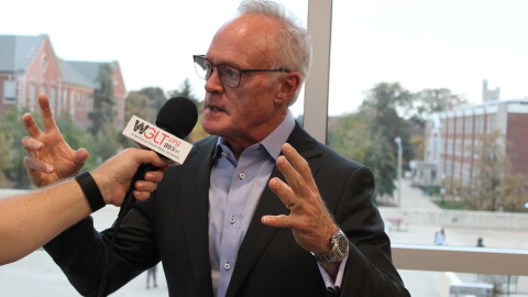 A man talks and gestures in front of a microphone 