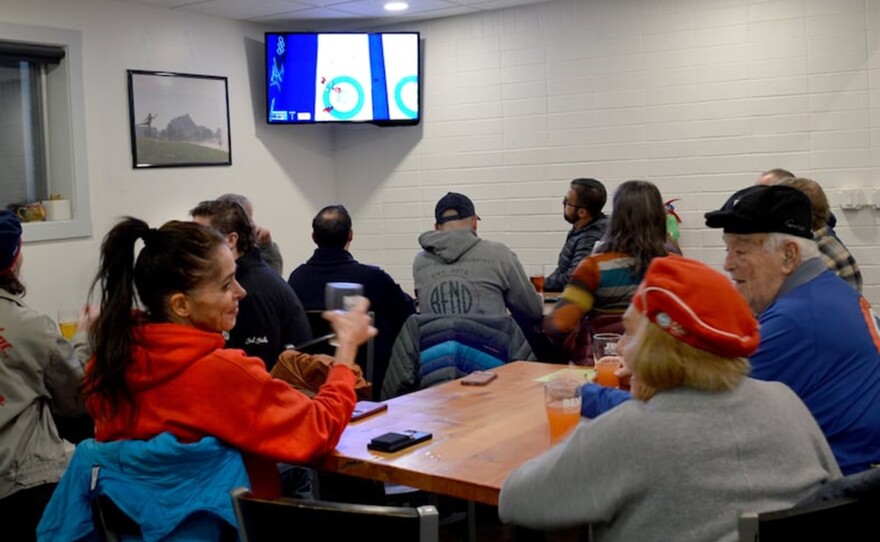 People watch curling on a tv together in a room.