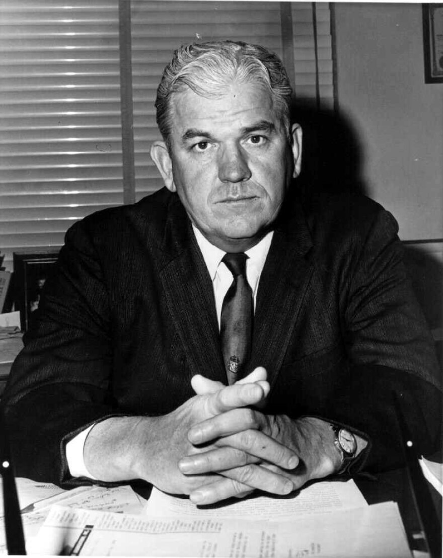 Dallas County District Attorney Henry Wade is seen in a black and white photo, sitting at a desk covered with papers.