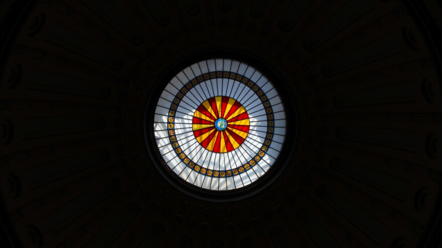Light shines through the round stained glass dome in the Ohio Statehouse rotunda. The rest of the photo is too dark to make out. 