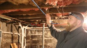 A worker with a headlamp reaches toward insulation on the low-hanging ceiling of the basement in a New Hampshire home.