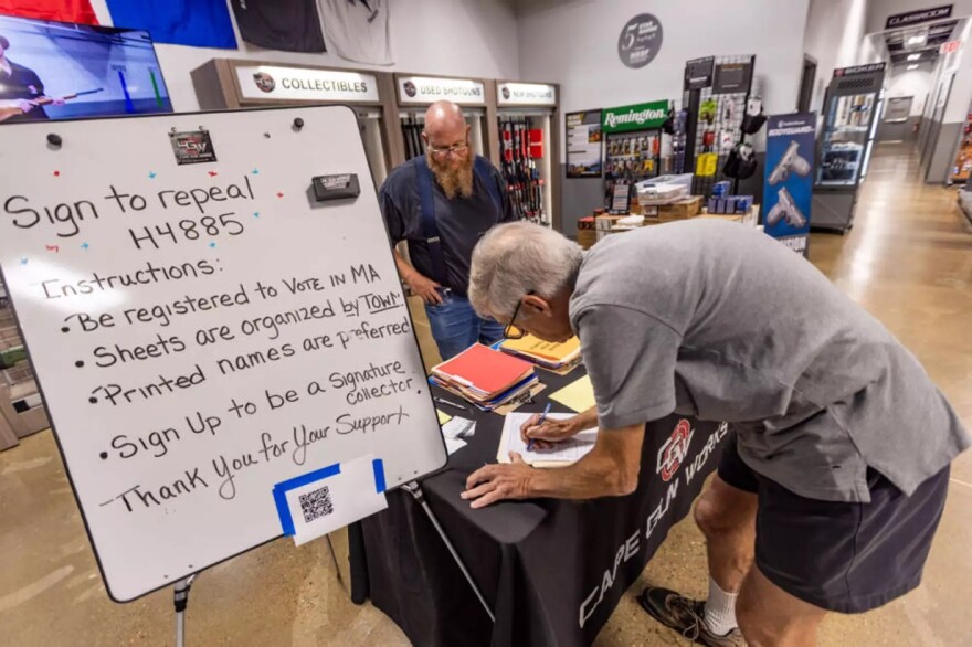 John Mawhinney, a civil rights coalition state field coordinator, watches as Martin Laspada, of Bourne, signs a petition to repeal the state's new gun reform law.