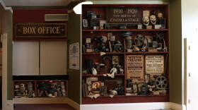 A wall display featuring vintage film equipment, posters and photographs beside a box office window.