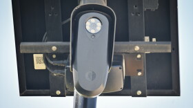 Outdoor, close-up photo of a small black camera attached to a small solar panel.