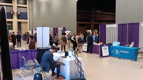 Attendees of the New York State Innovation Summit mingle in the section within the Buffalo Convention Center where booths were hosted by businesses and the state agencies that can help them with resources. Beyond the walls in the darkened section, a panel discussion was in progress.