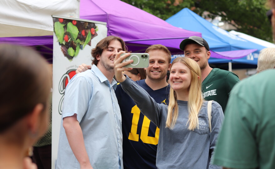 Photos of Josh and Jace, two young British men, taking photos with fans and mascots. The two are wearing a blue University of Michigan and a green Michigan State University jersey respectively.