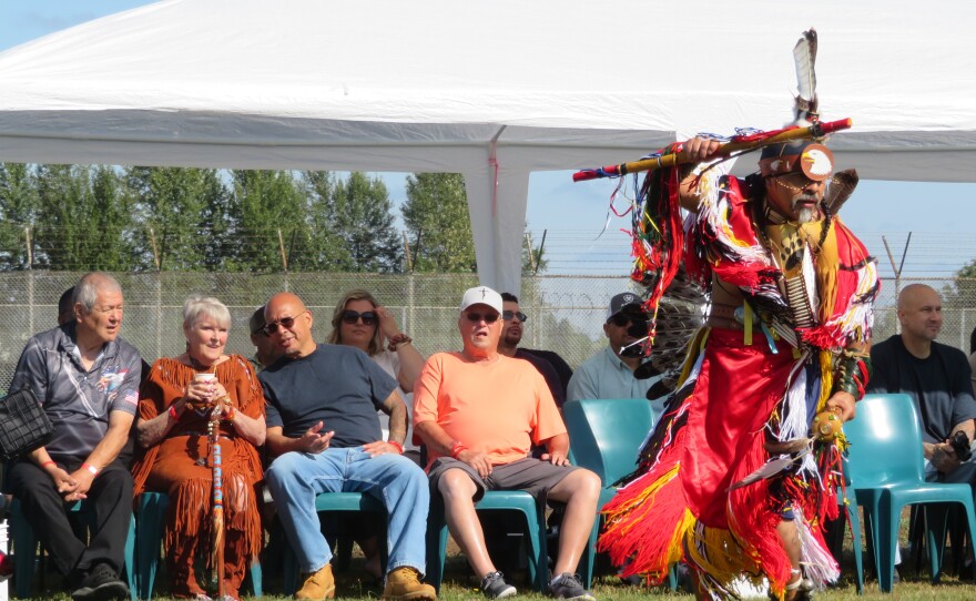 Man in powwow attire dancing before crowd. 