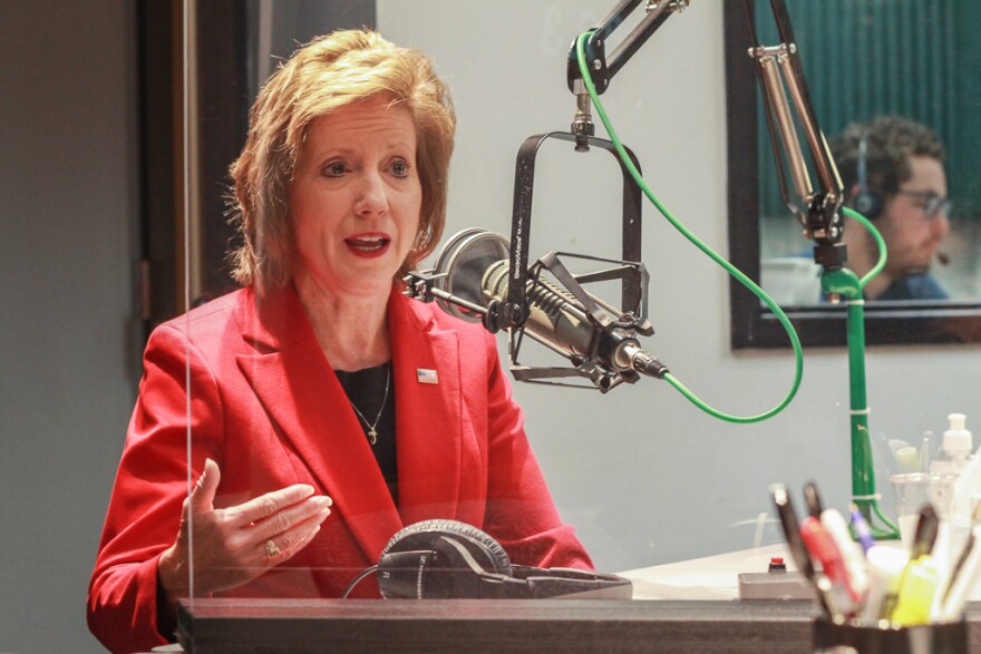 A woman in a red blazer sits behind a microphone in a radio studio.