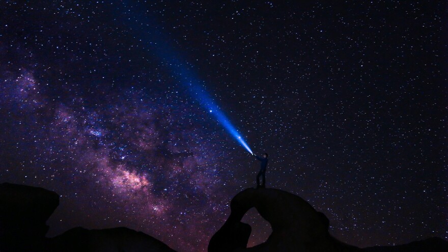 A person stands atop a rock formation while looking up at the stars.