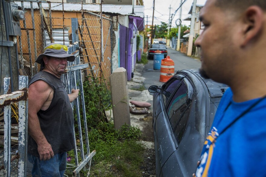 Angel Rosario,right, and Jose Contreras speak in front of Contraras' home as he takes a break from rebuilding it. (Jesse Costa/WBUR)