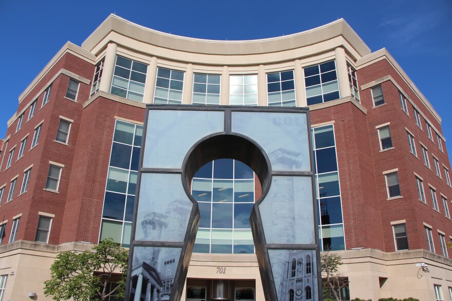 A photo of the exterior of the red brick Columbia government building. The key hole sculpture in front of the building is centered in the image. 